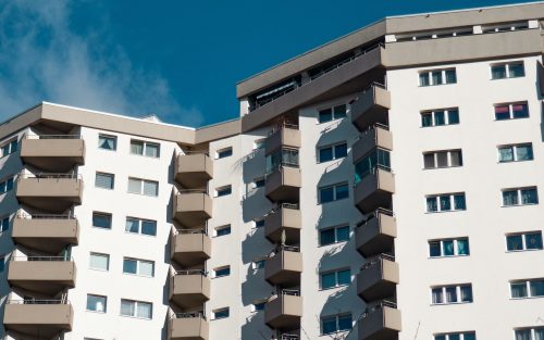 Ein weißes Mehrfamilienhaus welches vor einen blauen himmel ist.